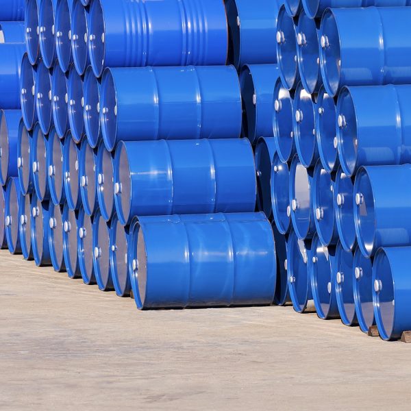 Piles of many blue oil drums stacked on industrial yard area